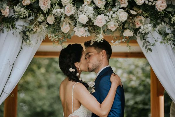 A photograph of a small cornish wedding, bride and groom are kissing after ceremony under an arbour