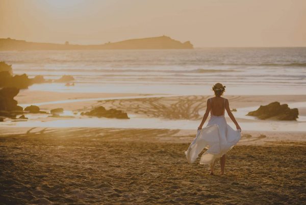 A photograph of a bride walking along a beautiful sandy beach at sunset a beautifully stylish beach wedding