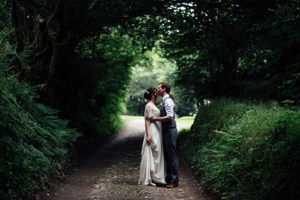 A photograph of a couple kissing under trees after their outdoor arbour wedding