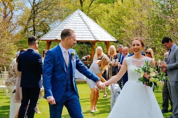 A photograph of a bride and groom walking down a magical natural aisle