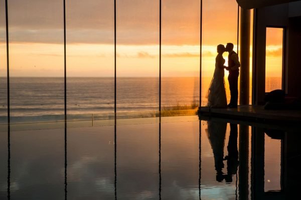 A photograph of a couple kissing by an infinity pool looking out to sea with a beautiful sunset. Style of photography natural reportage